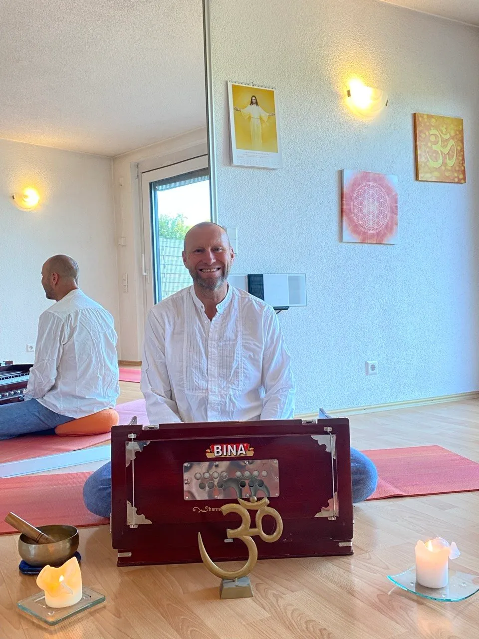 Christian Pfaff im weißen Hemd, lächelnd am Harmonium im Yogaraum